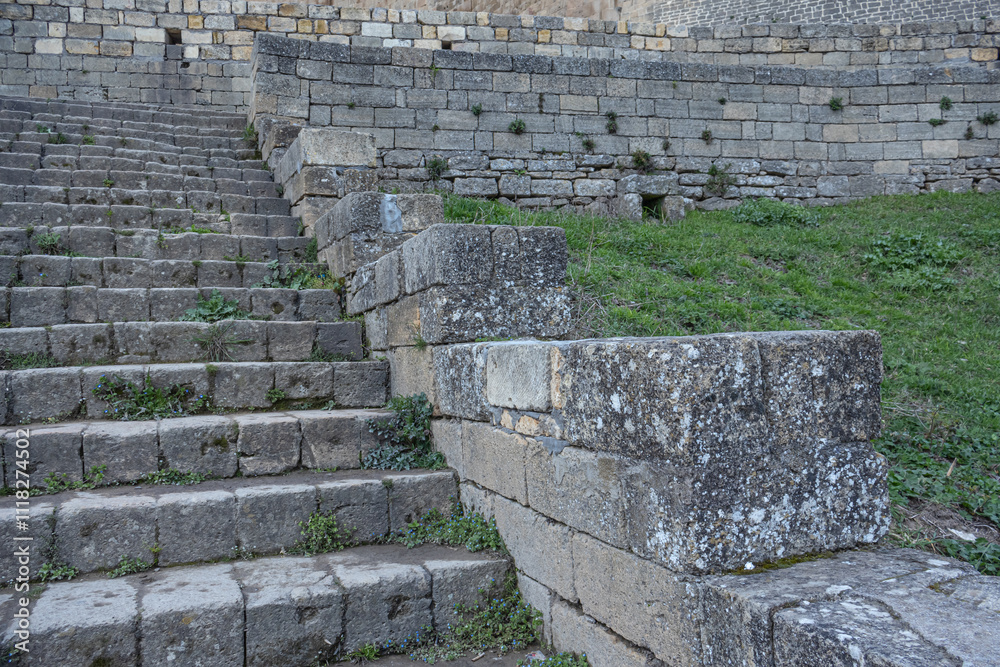 An ancient staircase made of large gray stone blocks. The background is made of stone blocks. The steps of the ancient staircase leading to the fortress. Grass grows between the stone blocks. An ancient staircase made of large gray stone blocks. The background is made of stone blocks. The steps of the ancient staircase leading to the fortress. Grass grows between the stone blocks.