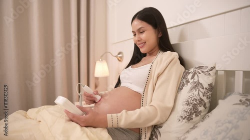 Pregnant woman holding pocket fetal doppler to listen baby heartbeat on belly