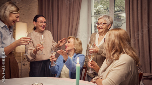 Canvas Print Emotional elderly women, friends meeting at home, in cozy living room, cheerfully talking, discussing news, drinking wine