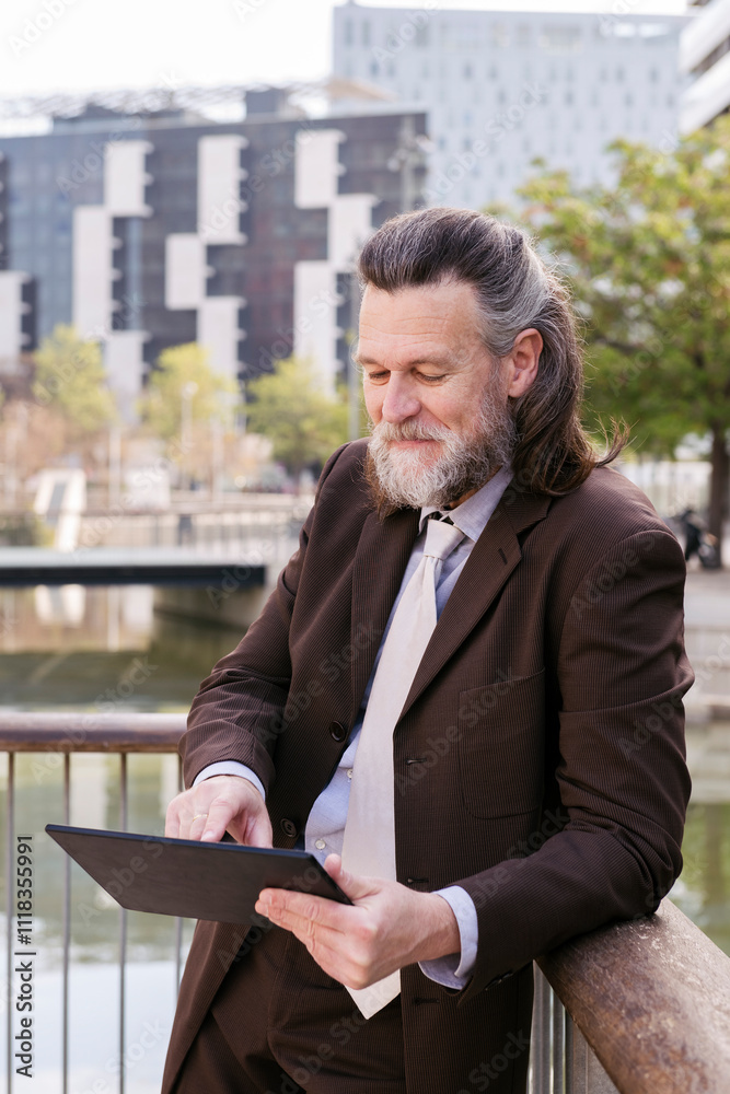 positive middle age male with beard in formal outfit browsing tablet while standing at city, concept of business and mature man lifestyle, copyspace for text