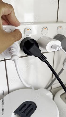 Hand Pressing Power Button on Wall Socket with Multiple Electrical Plugs and Power Strip