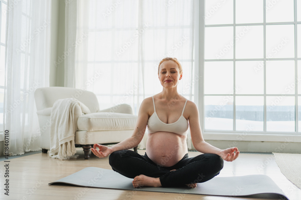 Fototapeta premium Pregnancy prenatal breathing. Pregnant woman with big belly sitting in lotus pose on yoga matt at home. Pregnant girl practicing yoga mindfulness meditation. Relaxation self care during pregnancy