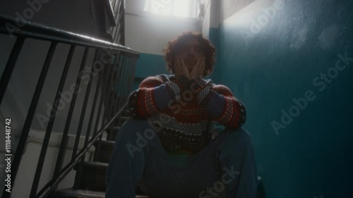 Full shot of distressed Caucasian man in sweater and jeans sitting alone in stairway and questioning meaning of life