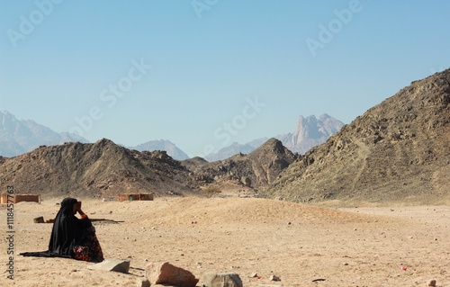 Bedouin woman in black paranja seating in the middle of rocky desert in Egypt. photo