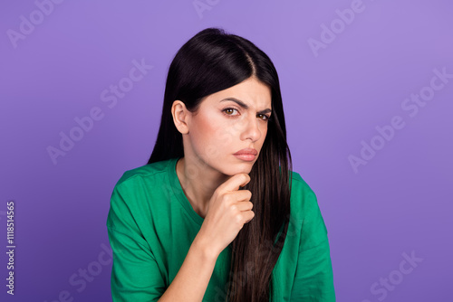 Young woman with thoughtful expression and hand on chin against vibrant purple background photo