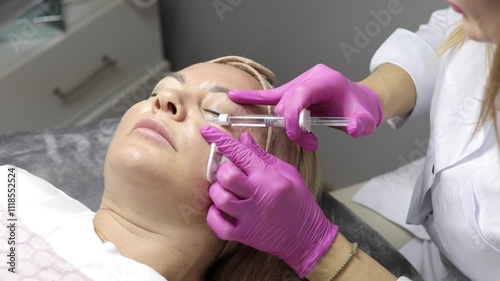 A cosmetologist gives injections into a patient's face