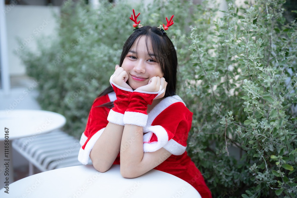 Portrait Cute Smiling asian girl in red santa with looking to the camera near Christmas greeting picture parcel decoration on Christmas tree background Decoration During Christmas and New Year.