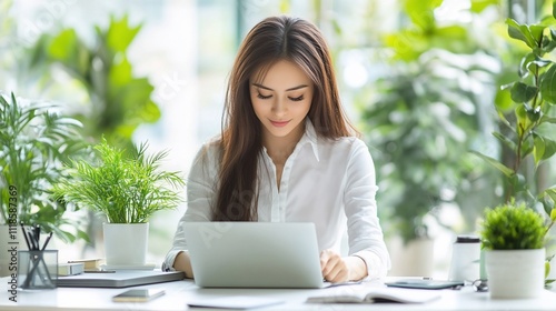 Focused young woman working on laptop in a bright, plant-filled office.