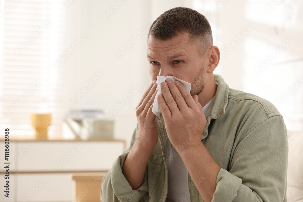 Man with tissue blowing runny nose at home. Space for text Man with tissue blowing runny nose at home. Space for text