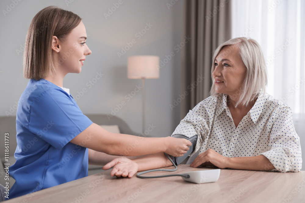 Obraz premium Healthcare worker measuring patient's blood pressure at wooden table indoors