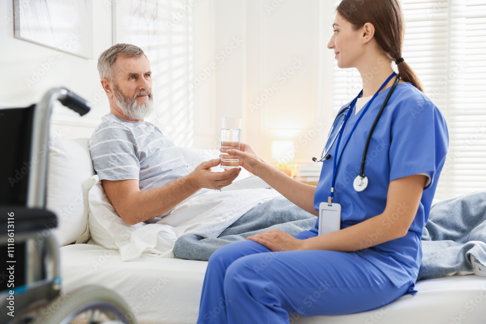 Caregiver giving water to senior man on bed indoors. Home health care service Caregiver giving water to senior man on bed indoors. Home health care service