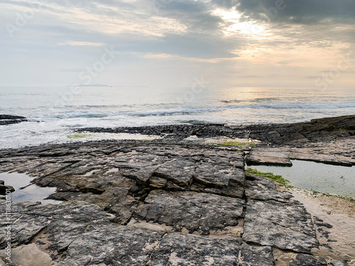 Rocky shoreline with gentle waves and tide pools at sunrise on UK coast