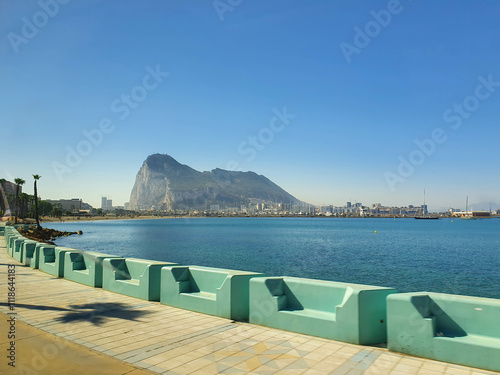 Gibraltar rock overseeing the seafront promenade with palm trees and benches on a sunny summer day