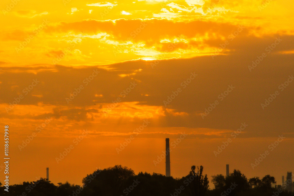 Dramatic sunset over industrial landscape creating a golden sky near a city skyline Dramatic sunset over industrial landscape creating a golden sky near a city skyline