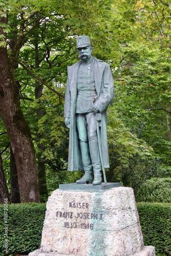 Innsbruck, Austria - September 30 2024: Bronze Statue of Emperor Franz Joseph I in Military Uniform and Overcoat, Set Against Green Trees in Park photo