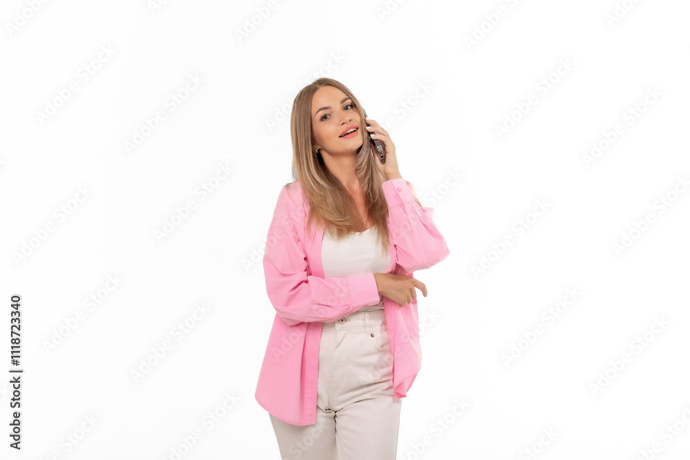 A young woman wearing a pink blouse smiles while talking on her smartphone against a plain white background A young woman wearing a pink blouse smiles while talking on her smartphone against a plain white background