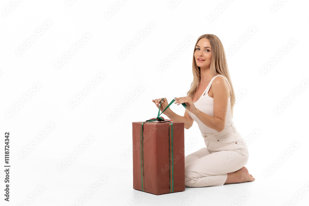 A woman kneeling on a bright background with a large gift, wrapping it carefully with a green ribbon A woman kneeling on a bright background with a large gift, wrapping it carefully with a green ribbon