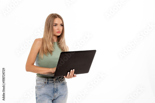 Young woman using a laptop while standing against a plain white background in a casual setting, focused on her task and engaged in work