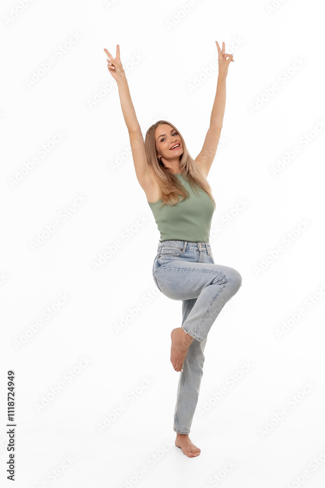Young woman joyfully posing with one leg raised and arms extended in a playful manner against a bright white background Young woman joyfully posing with one leg raised and arms extended in a playful manner against a bright white background