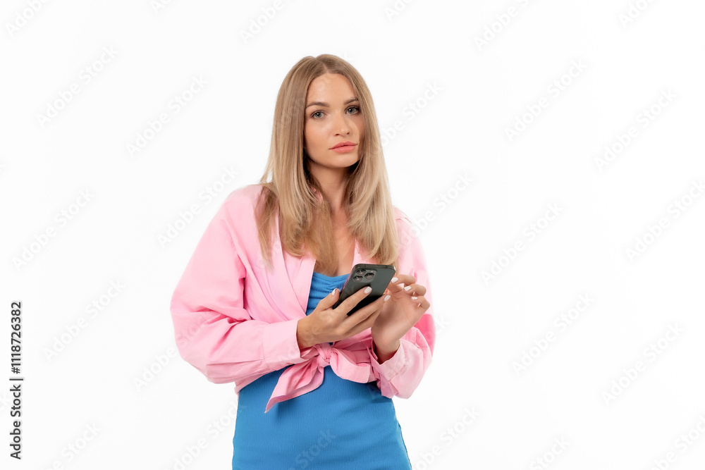 A woman in a pink shirt and blue dress holds a phone while posing against a white background in a studio setting A woman in a pink shirt and blue dress holds a phone while posing against a white background in a studio setting