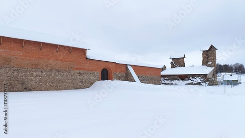 The 14th century castle was built of stone and red brick and has become a ruin. It is currently being restored Next to the castle there is a lawn, trees and houses Cloudy winter weather and snow