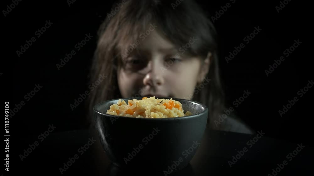Homeless child with food indoor. A homeless little girl with smile look at the meal in the bowl against black background. Homeless child with food indoor. A homeless little girl with smile look at the meal in the bowl against black background.