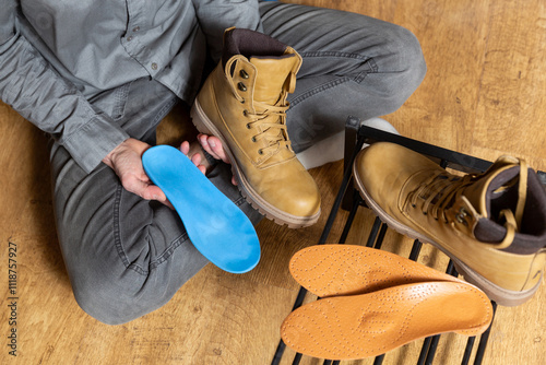 Close up of man hands putting custom  orthopedic insoles insider yellow boots on a gray background. photo