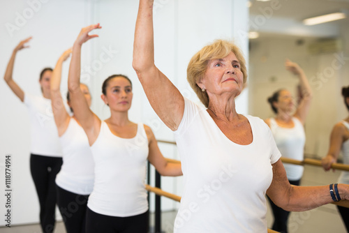 Group of ballerina standing with one hand on barre and reaching over hand in bright fitness room photo