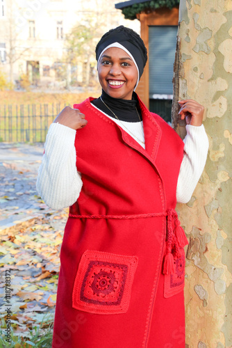 In a city park, a black woman with dimples in her cheeks, wearing ethnic red boho clothes, smiles charmingly.