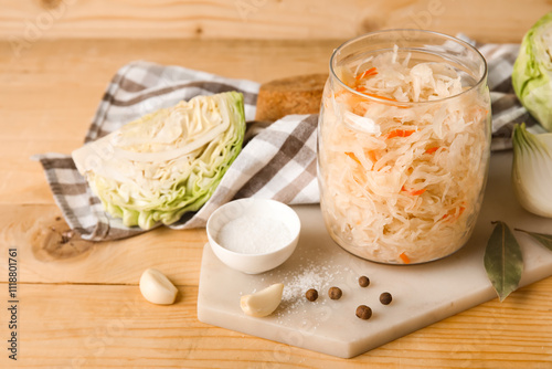 Delicious sauerkraut in jar with ingredients on wooden background