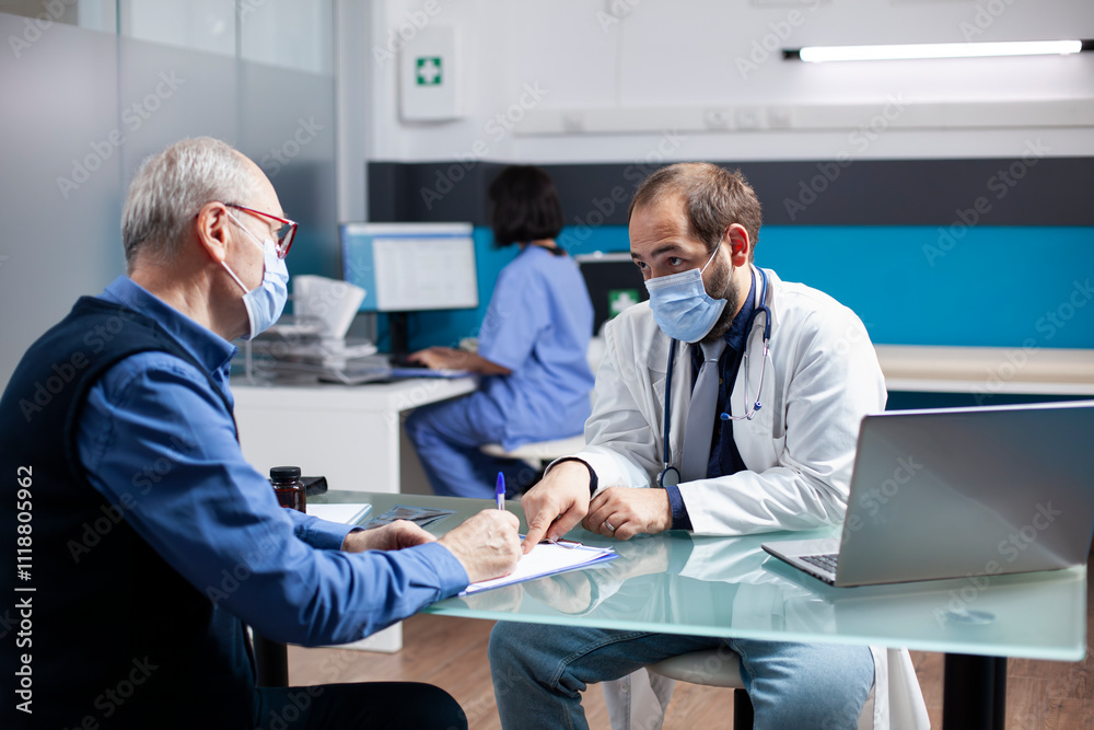 General practitioner aids elderly caucasian man in filling out medical information on clipboard. Young doctor and male pensioner, both wearing masks, discussing health assessment in clinic office. General practitioner aids elderly caucasian man in filling out medical information on clipboard. Young doctor and male pensioner, both wearing masks, discussing health assessment in clinic office.