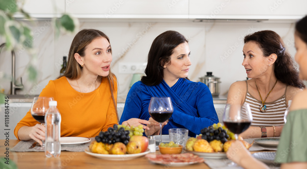 Cheerful female friends enjoying home gathering with wine and light snacks at kitchen table, engaging in lively conversations.. Cheerful female friends enjoying home gathering with wine and light snacks at kitchen table, engaging in lively conversations..