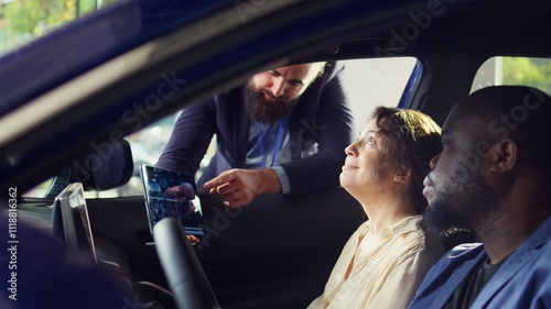 Showroom salesperson showing stat charts on tablet to clients after they finished test drive to persuade them. Dealership agent showing vehicle driving metrics graphs on device to couple, camera B photo