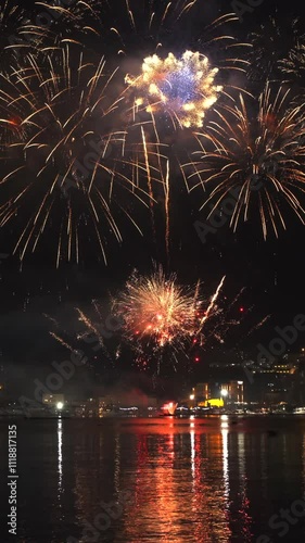 Bright fireworks exploding with colorful lights over sea shore and small mediterranean town. Vertical video