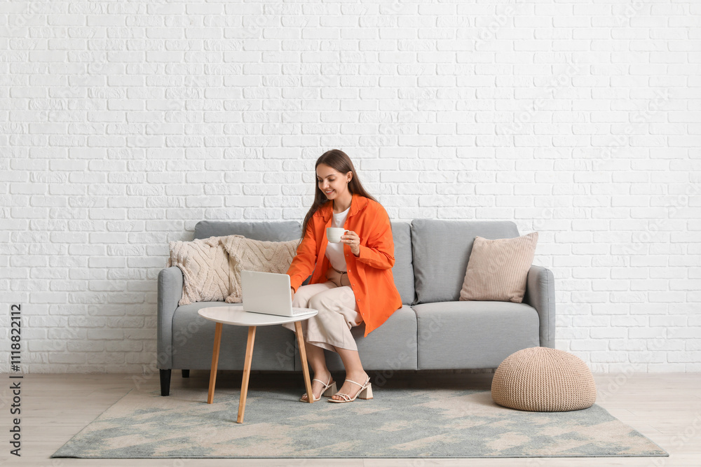 Young pretty woman chatting with laptop at coffee table and sitting on grey sofa at home Young pretty woman chatting with laptop at coffee table and sitting on grey sofa at home