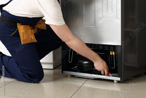Fotografie Male worker repairing refrigerator in kitchen, closeup