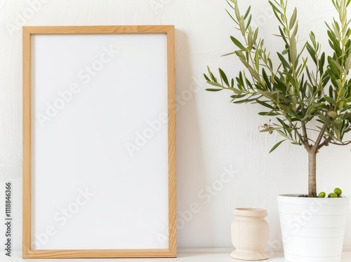 Blank picture frame with a potted olive tree on a white shelf against a white wall