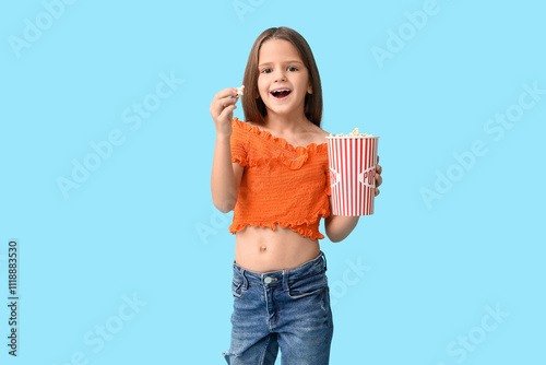 Happy little girl with popcorn on blue background