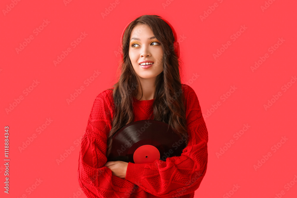 Beautiful young Asian woman in stylish sweater and modern headphones with vinyl disk on red background Beautiful young Asian woman in stylish sweater and modern headphones with vinyl disk on red background