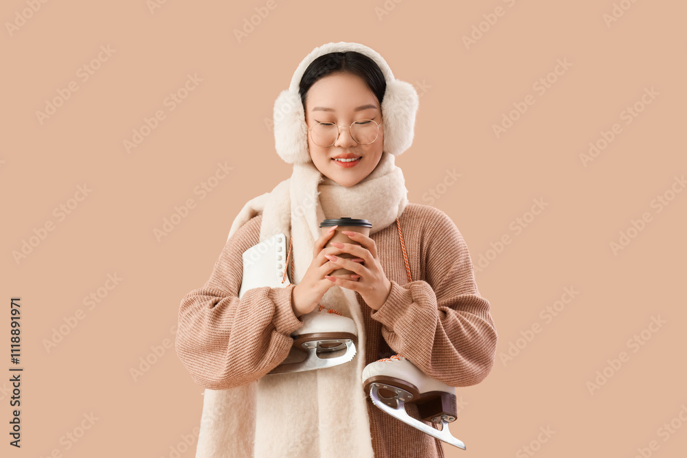 Beautiful young happy Asian woman with ice skates and cup of coffee on beige background