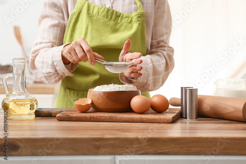 Obraz na plátně Woman sifting flour for preparing dough on kitchen counter