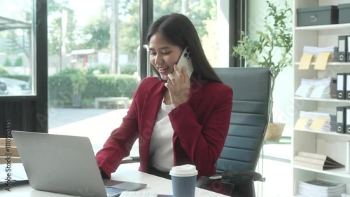 A young Asian woman works diligently at her desk in a bright office room during the day. Surrounded by files, charts, and devices, she strategies on marketing funnels and SEO optimization.