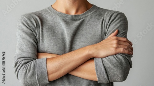 A person with crossed arms, wearing a gray sweater against a neutral background.