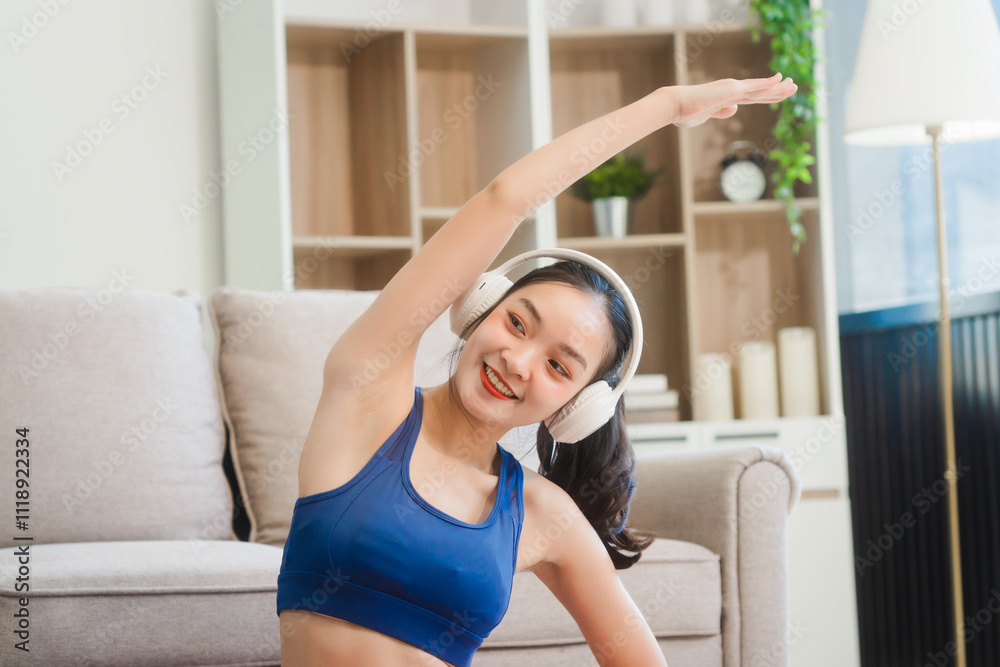 A young Asian housewife sits on sofa in her living room, using fitness app on her mobile with headphones. dumbbells and whey protein, she balances yoga, workouts, vegetarian diet and weight loss. A young Asian housewife sits on sofa in her living room, using fitness app on her mobile with headphones. dumbbells and whey protein, she balances yoga, workouts, vegetarian diet and weight loss.