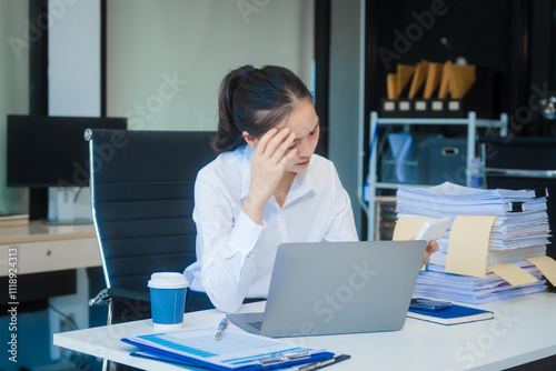 Foto A young Asian businesswoman works alone at a desk under daylight with a laptop, papers, and documents