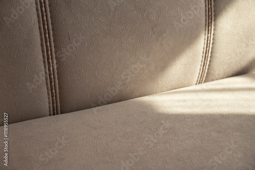 Soft beige velour sofa quilted with straight lines of stitching in shadows and sunlight. Part of the sofa with a soft back and seat close-up with copy space.