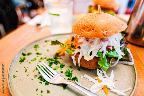 Close-Up of a Fresh and Delicious Vegetarian Burger with Shredded Vegetables and Leafy Greens on a Plate with Decorative Parsley Garnish in a Casual Dining Setting
