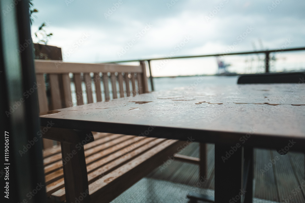 Wooden Bench and Table on Balcony with Raindrops Suggesting a Tranquil and Calming Atmosphere in an Outdoor Setting Overlooking a Cloudy Sky and Scenic View of the Waterfront Wooden Bench and Table on Balcony with Raindrops Suggesting a Tranquil and Calming Atmosphere in an Outdoor Setting Overlooking a Cloudy Sky and Scenic View of the Waterfront