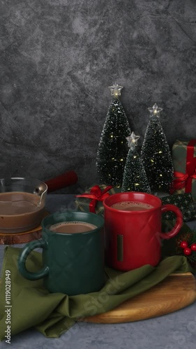 Red and green hot chocolate mugs and small Christmas tree. Sweet drink with cocoa and milk. A cozy homemade Christmas Eve evening