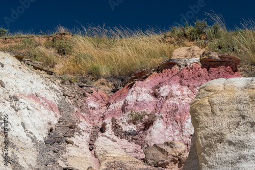 Colorful rock formations and vibrant grasses at a geological site during sunny daylight in an expansive landscape of natural beauty and geological diversity photo